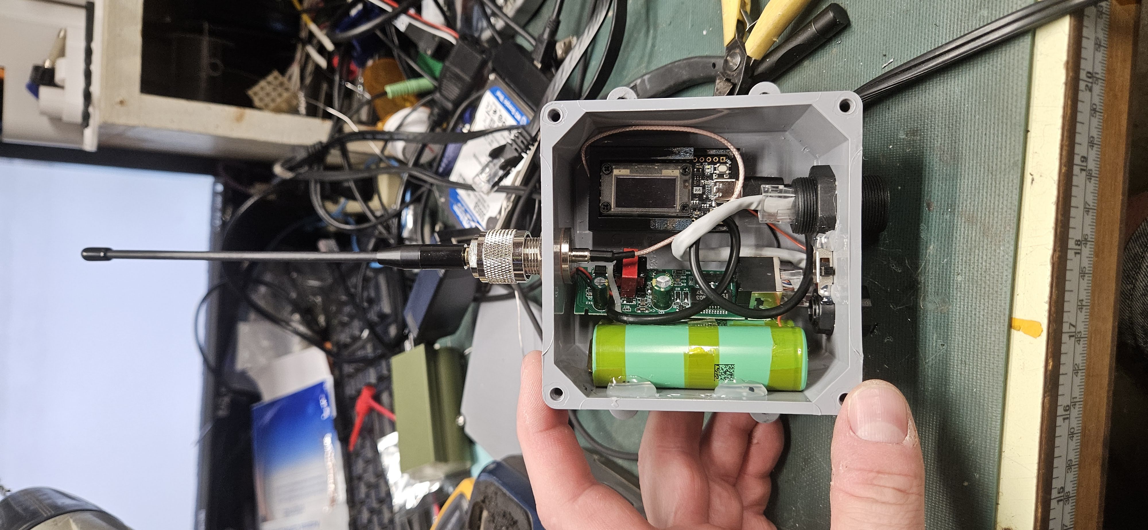Bench prototype showing open PVC box with internal component layout, battery, decased PoE board, and Heltec board